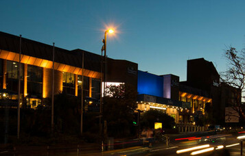 The exterior of Bournemouth International Centre illuminated at night, with warm lighting and light trails from passing traffic.