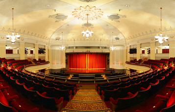 Interior of Bournemouth Pavilion Theatre, featuring a grand red-curtained stage, ornate ceiling, and rows of plush red seating in a classic theatre layout.